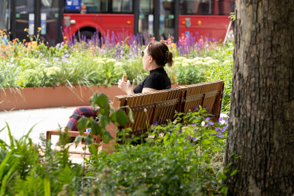 Lady sitting on AKRI 600 bench and planter eating lunch at Strand