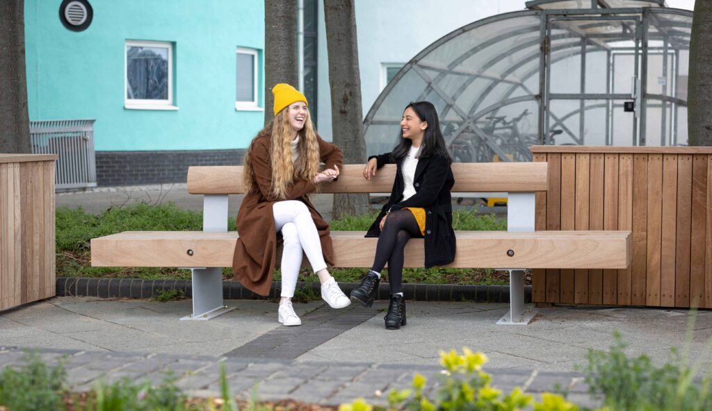 Two students chatting on a fordham bench at UEL docklands campus